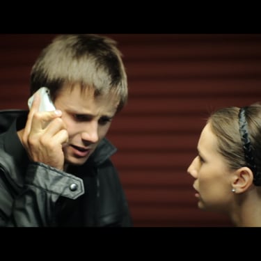 A young man with a worried look on his face talks on a mobile phone as his girlfriend watches on