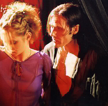 A beautiful young woman is led into a room by a sinister looking man wearing black