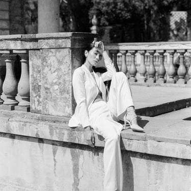 A classic woman sitting on a ledge in a minimalist suit.