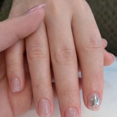 Diseño de uñas natural estilo 'Clean Girl' con base nude, destellos sutiles de glitter y detalle de estrella plateada