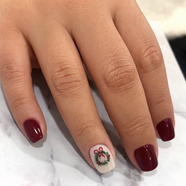 Manicura de Navidad elegante en color vino tinto con detalle de corona de muérdago y lazo rojo
