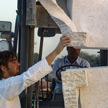 Sculptor Roberto Manzano inspects a white marble sculpture being moved outdoors by a forklift operator.