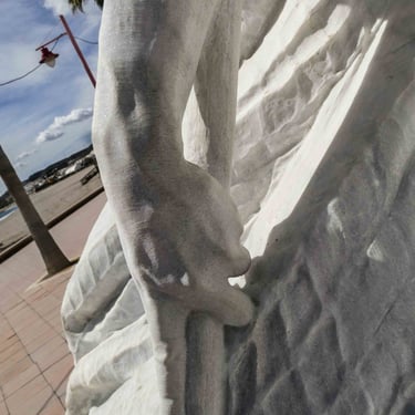 Detail of a marble sculpture of a hand and a fishing net by the sea.