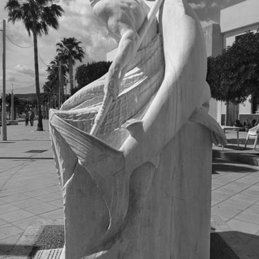 Marble sculpture of a fisherman holding a swordfish and a hook on a seafront promenade.