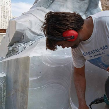 Sculptor with hammer in hand working on a half-finished marble sculpture of a man.