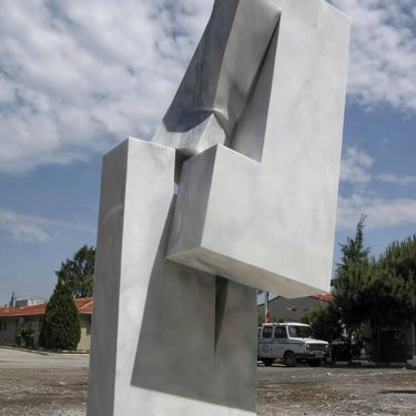 Modern geometric marble sculpture with interlocking white stone blocks under a blue sky.