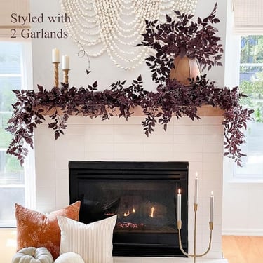 Fall fireplace decor with faux burgundy leaf garlands, cozy throw pillows, and taper candles