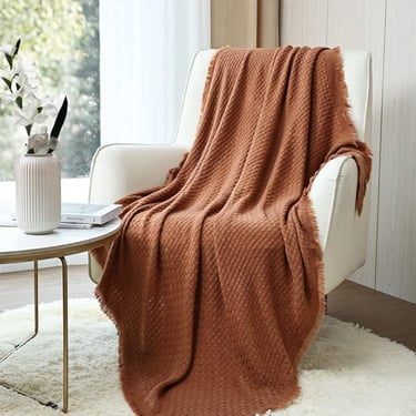 Rust-colored textured throw blanket draped over a white armchair in a modern, cozy living space