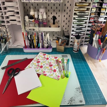 Desk with a variety of craft tools, paper, scissors, ruler and various writing tools. 