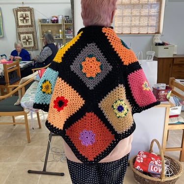 A brightly coloured women's crocheted shawl viewed from behind.