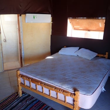 Letto matrimoniale, finestra, aria condizionata e porta aperta sul bagno nel bungalow.