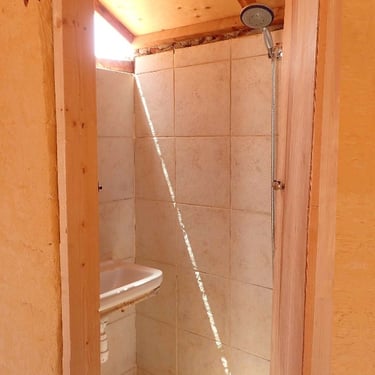 Bagno compatto di 90cm x 3m con piccolo lavandino e doccia nel bungalow.