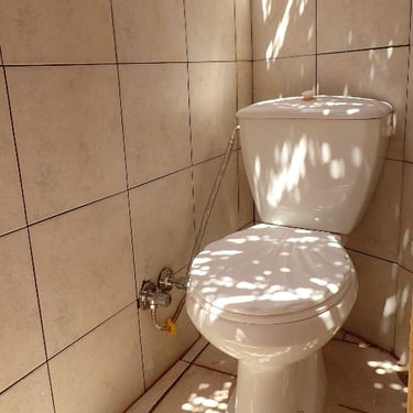 WC bianco chiuso circondato da piastrelle su pavimento e parete nel bungalow.