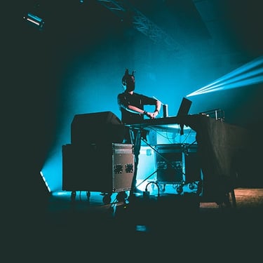 Vagues de lumières colorées projetées sur un DJ en pleine immersion dans son mix, capturées par Thomas Bordas.