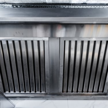 A commercial stainless steel kitchen exhaust hood with parallel slats for air filtration.