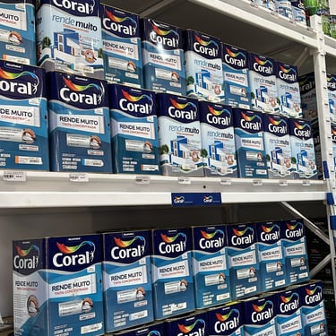 Diversas latas de tinta em uma prateleira da Bocalan Materiais para Construção, apresentando uma ampla variedade de cores e a