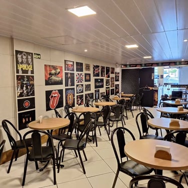 Área da cafeteria com mesas cadeiras e pôsteres de rock no Studio Brothers em Porto Alegre