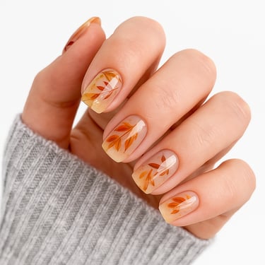a women's hand with autumn leaf press on nails an a grey sweater