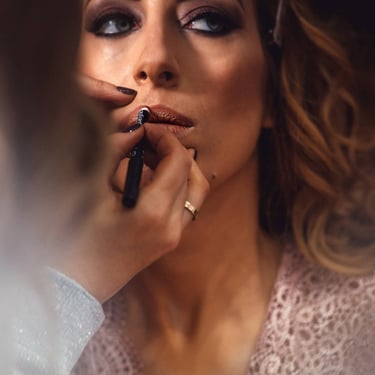 Le mani di una Makeup artist mentre da un tocco finale di matita sulle labbra della sposa ritratta in foto