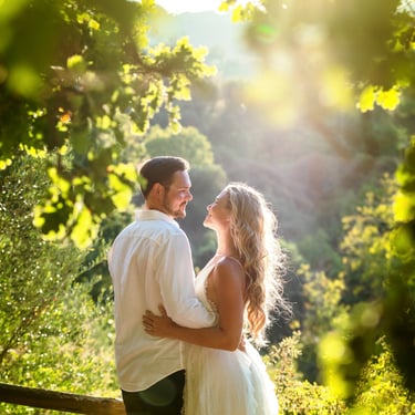 Due sposi si abbracciano e si scambiano sguardi profondi tra gli alberi illuminati dal sole forte pomeridiano