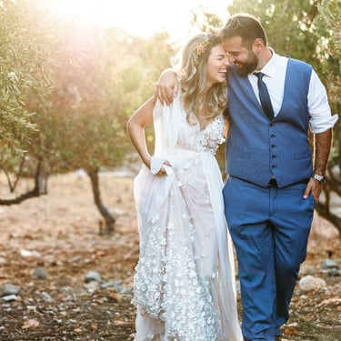 Una coppia di sposi cammina tra gli ulivi abbracciandosi e ridendo allegramente