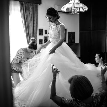 Le persone più vicine alla sposa la aiutano a sistemare la gonna del suo abito composta da diversi veli