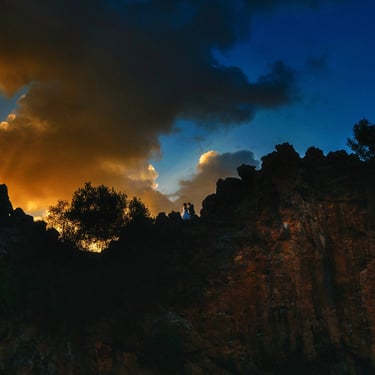 Un tramonto in montagna, gli sposi si abbracciano, dietro di loro un cielo blu e una luce calda che colora una grossa nuvola