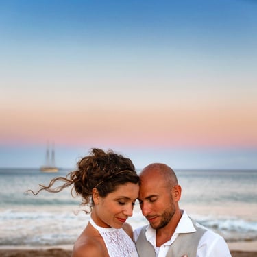 Due sposi si abbracciano al tramonto, dietro di loro una barca a vela naviga il mare dell'sola greca di Antiparos