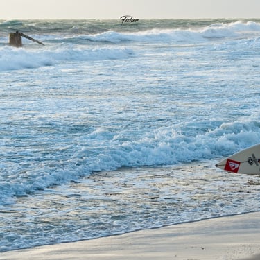 A young man runs with surfboard under his arm looks at broken pylon at Cottesloe Beach near sunset