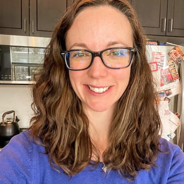 Headshot of Dee wearing glasses and smiling at the camera