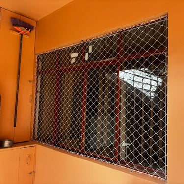 Janela ampla com rede de proteção instalada, parede laranja ao redor.