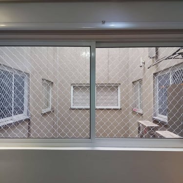 Janela interna com tela de segurança instalada, olhando para pátio interno do prédio.
