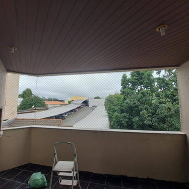 Varanda de apartamento com tela de segurança instalada, forro de madeira e vista externa nublada.
