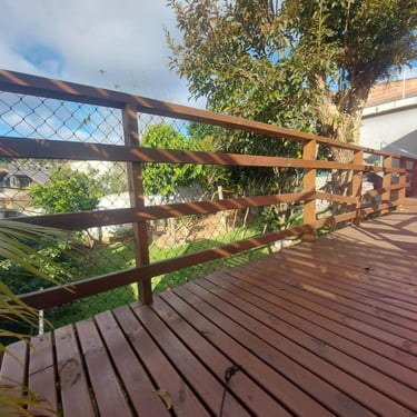 Deck de madeira com guarda-corpo e rede de proteção, jardim ao fundo.