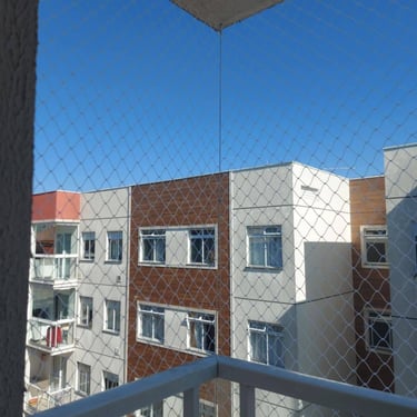 Sacada de apartamento com rede de proteção, prédios ao fundo e céu azul.