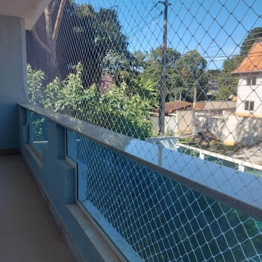 Sacada com rede de proteção e guarda-corpo azul, vista para árvores e casas.