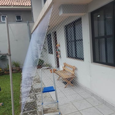 Malha de segurança esticada do beiral ao piso na área externa da casa.