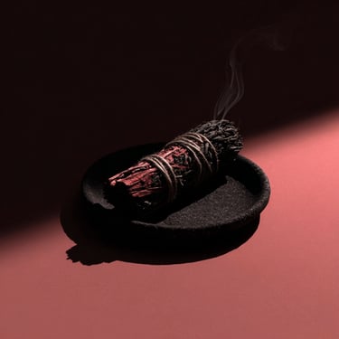 A stick of burning incense with a faint, elegant wisp of smoke rising into a solid black background