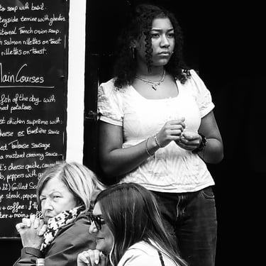 A woman stands in the doorway of a restaurant, looking a bit bored. The Grassmarket, Edinburgh