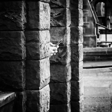 A pair of man's hands holding a phone poke out from the doorway of a church at Holy Corner, Edinburgh
