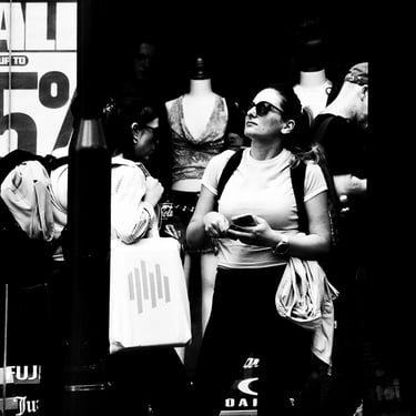 A woman stands at a bus stop, looking up at the departure board on Princes Street, Edinburgh