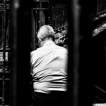 A man sits in St Cuthbert's Kirkyard, framed between two railings Lothian Road, Edinburgh