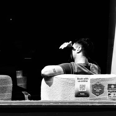 A man shields his face from the sun as he sits in shadow at a cafe window on West Maitland Street, Edinburgh