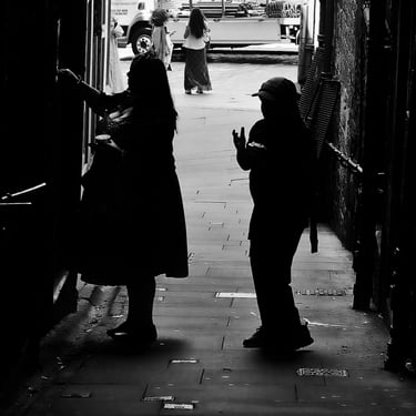A woman and child, in shadow, stand at a stair door in a close off The High Street, Edinburgh