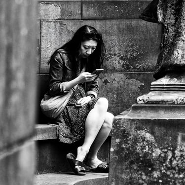 A woman sits scrolling on her phone in Princes Street Gardens