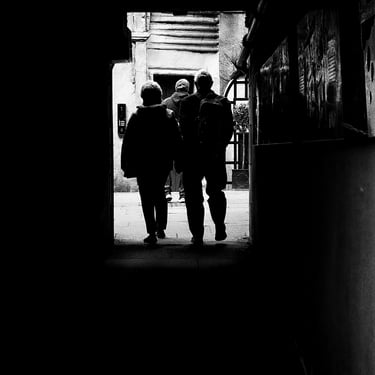 A couple emerge from a shadowy close into a courtyard. The High Street, Edinburgh