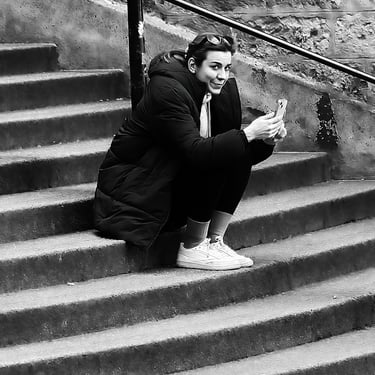 A woman on her phone, looking at me as I take her picture sitting on the steps of Advocate's Close, by Cockburn Street