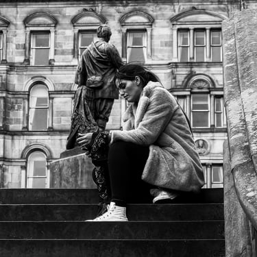 A woman, on her phone, sits on the steps near The Scott Monument, East Princes Street Gardens, Edinburgh