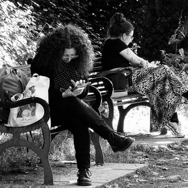 Two women sit on benches engrossed in their phones. Water of Leith Walkway, near St Bernard's Well, Edinburgh