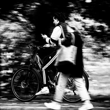 A cyclist, on the phone, freeze framed behind a blurred woman on Bruntsfield Links, Edinburgh